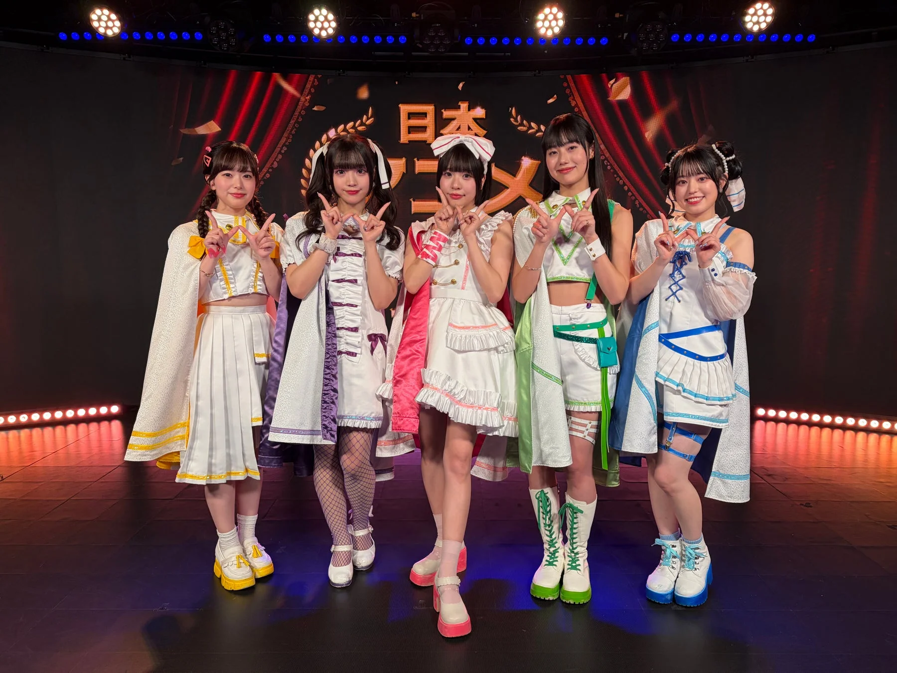 ステージ上で笑顔でVサインをする5人の女性アイドルグループ