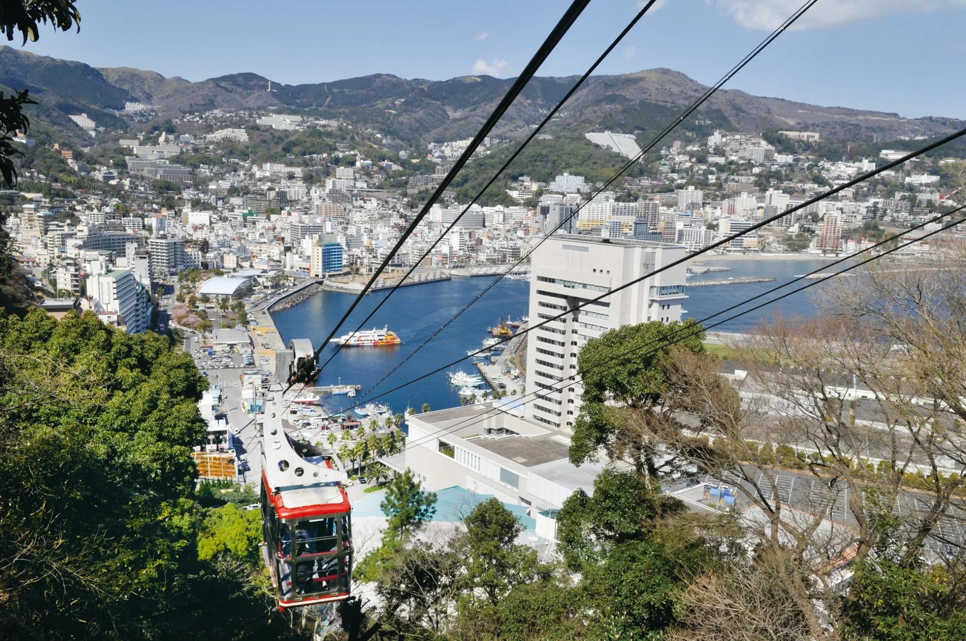 晴れた日に山から見下ろした港町の全景と赤いロープウェイ
